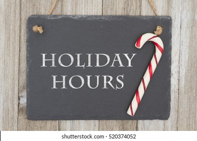 Old Fashion Christmas Store Message, A Retro Chalkboard With A Candy Cane Hanging On Weathered Wood Background With Text Holiday Hours