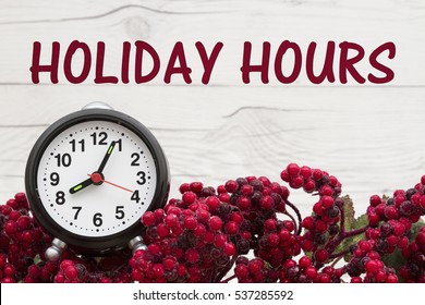 Old Fashion Christmas Store Message, Frost Covered Red Holly Berries With An Alarm Clock On Weathered Wood Background With Text Holiday Hours