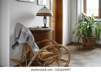 Old Fashion Wicker Rocking Chair With Blanket In Cozy House, Lamp On Wooden Cabinet. Place For Reading, No People, Home Plant Near Window. Comfortable Vintage Living Room Interior