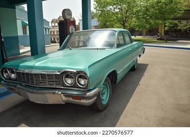 An Old Fashioned American Green colored car resembling Chevrolet Impala parked near a petrol Bunk against a green background.
