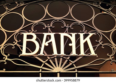 Old Fashioned Bank Sign With Ornamental Wrought Iron And Golden Letters. Building Exterior Of A Bank. Finance Symbol. 