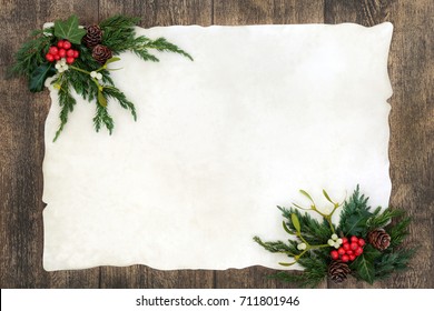 Old Fashioned Christmas Background Border With Holly, Mistletoe, Ivy, Juniper Fir And Pine Cones On Parchment Paper Over Old Oak Wood.