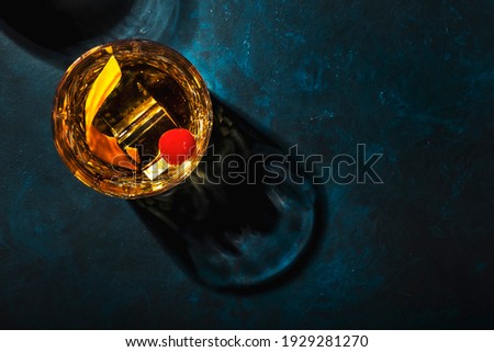 Old fashioned cocktail with bourbon whiskey, cherry and orange peel garnish, blue table, copy space, top view