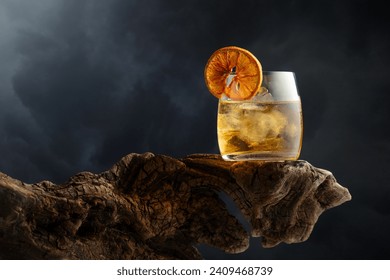 Old fashioned cocktail with ice and dried orange slice on a old wooden snag. Cold drink on a  background of cloudy sky. - Powered by Shutterstock