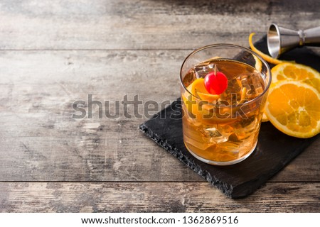Old fashioned cocktail with orange and cherry on wooden table. Copyspace