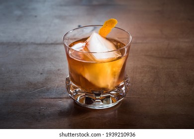 Old Fashioned Cocktail With Whiskey On A Wood Table With Orange Twist In An Elegant, Retro Crystal Glass Tumbler