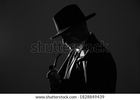 Old fashioned detective with smoking pipe on dark background, black and white effect