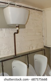 Old fashioned high level cistern feeding into urinals in a run down gents toilet or rest room