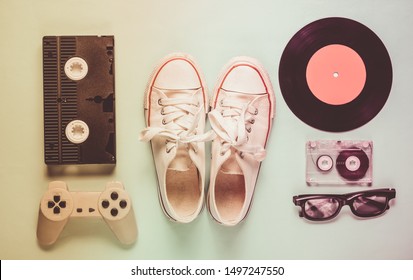 Old fashioned pop culture attributes from 80s on mint color background. Old sneakers, gamepad, audio cassette, videotape, vinyl plates, 3d glasses. Minimalism, top view