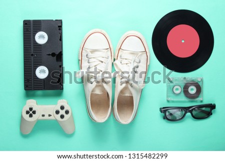 Old fashioned pop culture attributes from 80s on mint color background. Old sneakers, gamepad, audio cassette, videotape, vinyl plates, 3d glasses. Minimalism, top view