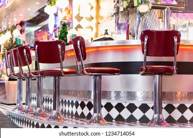 Old Fashioned Red Bar Stools In American Burger Retro Diner Restaurant. Interior Of Bar Is In Traditional American Style. Long Bar Counter.