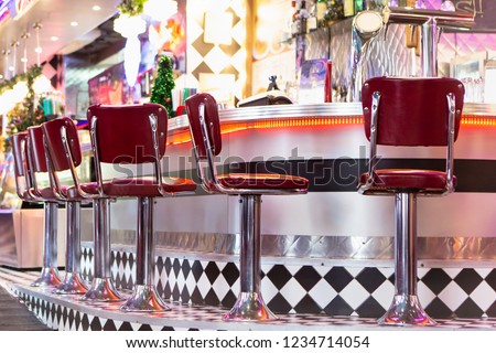 Old Fashioned Red Bar Stools In American Burger Retro Diner Restaurant. Interior Of Bar Is In Traditional American Style. Long Bar Counter.