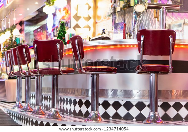 Old Fashioned Red Bar Stools In American Burger\
Retro Diner Restaurant. Interior Of Bar Is In Traditional American\
Style. Long Bar Counter.