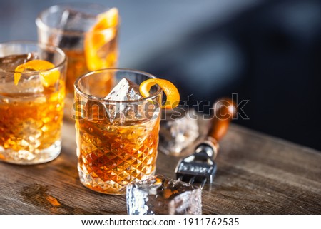 Old fashioned rum drink on ice with orange zest garnish.