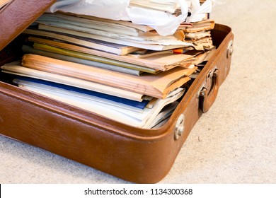 Old fashioned suitcase made of leather is full of folders, papers and documents, overloaded.