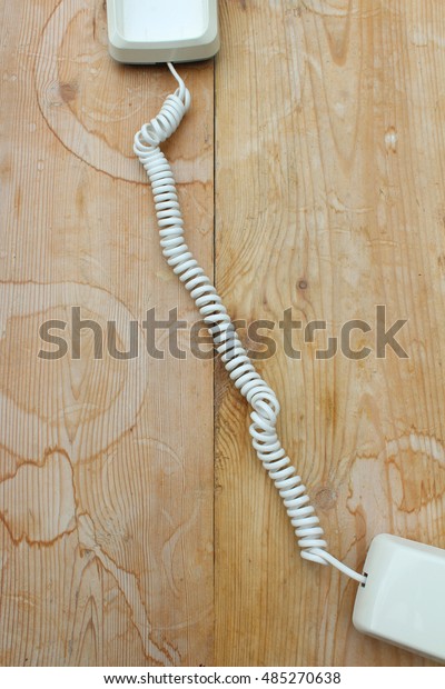 Old fashioned telephone cord and phone\
stretched across a weathered wood\
table.