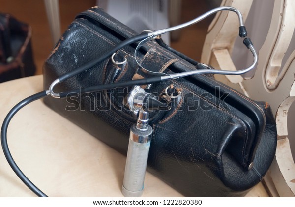 An old fashioned or vintage doctor\'s bag,\
stethoscope and otoscope on a\
chair.