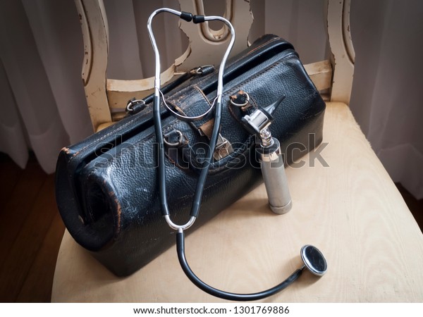 An old fashioned or vintage doctor\'s bag,\
stethoscope and otoscope on a worn\
chair.