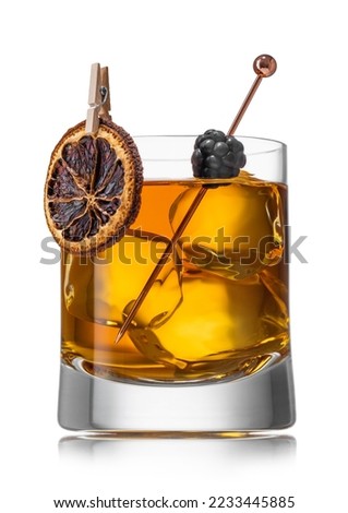Old fashioned whiskey cocktail with dry orange and blackberry and large ice cubes on white.