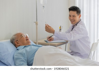 An Old Fat Asian Man With White Hair Wearing Eyeglasses And Light Blue Shirt Lay Down On The Bed In Hospital Room While Male Doctor With Short Black Hair Wearing White Lab Coat Smiling Checking 