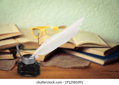 Old Feather Quill Ink Pen With Inkwell And Old Books On Wooden Desk