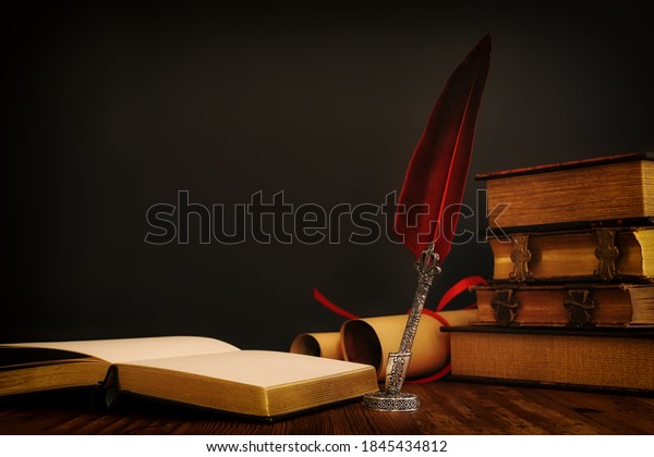 Old feather\
quill ink pen with inkwell and old books over wooden desk in front\
of black wall background. Conceptual photo on history, fantasy,\
education and literature\
topic.