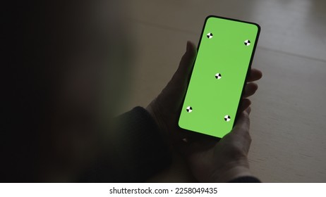 old female hands holding smartphone with green screen over wood vintage table with dim window light - Powered by Shutterstock