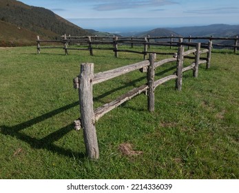 Old fence made out of wood and lush green meadow with valley and mountains in the background.