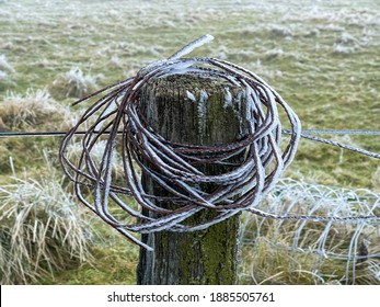 An Old Fence Post In The UK Peak District National Park With Rusty Coiled Wire For Fencing On It. On A Cold Winters Morning It Is Covered With Ice.