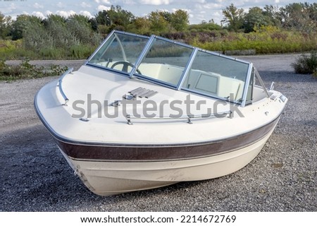 An old fiberglass runabout motorboat washed up or abandoned on a road