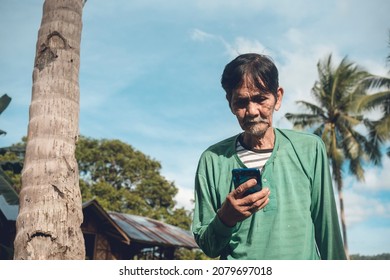 An old Filipino farmer checks his social media. Tech savvy senior citizen. Rural village scene