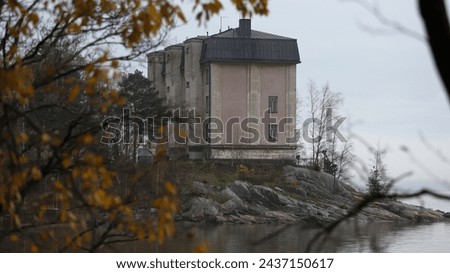 Old Finnish building on the island behind the tree branches, view from the Korkeasaari zoo island.