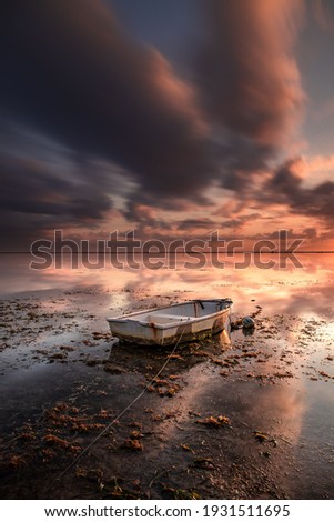 Old fisherman boat. Seascape. Fishing boat at the beach during sunrise. Low tide. Water reflection. Cloudy sky. Slow shutter speed. Soft focus. Vertical layout. Sanur beach, Bali, Indonesia.