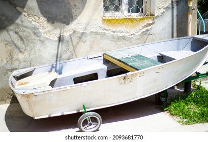 An Old Fishing Boat Moored By A Cement Wall With A Window. The Wheel Is Under The Boat.