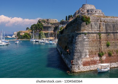 The Old Fortress Of Corfu On The Greek Island. Boys Jump Into The Blue Sea From Stone Walls. The Northern Side Of Contrafossa Opening To The Gulf Of Kerkyra.