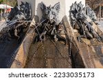 Old fountain decorated with gargoyle heads emitting thin trickles of water on sunny day in park