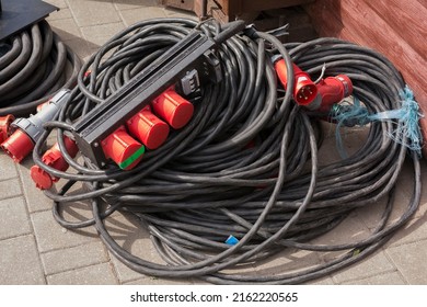 An Old Frayed High-voltage Wire With Red Sockets And Protective Devices Lies On The Asphalt