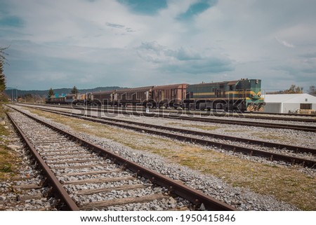 Old freight train with old and noisy diesel engine. Mixed waggons on a cloudy day.
