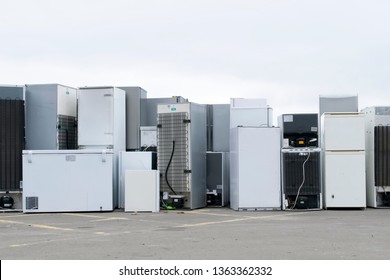 Old fridges freezers refrigerant gas at refuse dump skip recycle stacked pile plant help environment reduce pollution white silver 