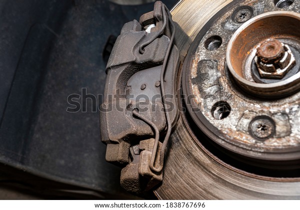 Old\
front brake disc with caliper and brake pads in the car, on a car\
lift in a workshop, close-up of a brake\
caliper.