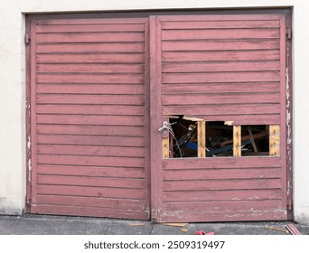 Old garage with two weathered  red doors, where one of it is broken, clearing the sight to a pile of junk inside. Door handle is fixed with a cable. Symbol of decay and not caring. - Powered by Shutterstock