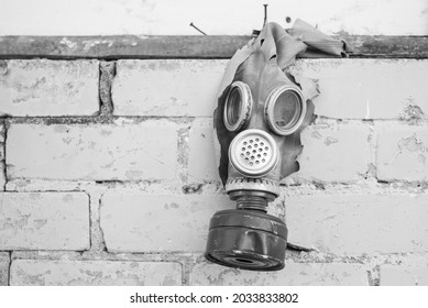 Old gas mask with coal filter hung on the brick wall. Black and white. Concept - Nuclear Disarmament and Radiation Protection, epidemic, coronavirus, covid-19, pandemic.