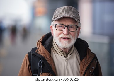 Old Generation. Portrait Of Positive Senior Bearded Man With Glasses Is Standing Outdoors And Looking At Camera With Slight Smile