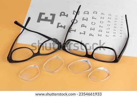 Old glass lenses in front of newly changed shortsighted reading eyeglass lenses with blurred paper of Snellen eye test chart on bright yellow background
