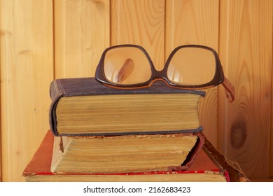 Old Glasses With Thick Lenses Lie On Old Books. The Concept Of Damage To Eyesight Reading Books.