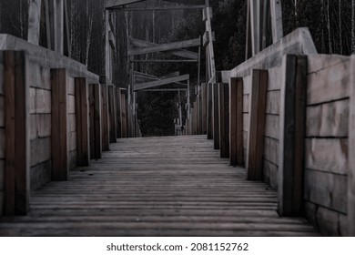 Old and gloomy wooden bridge over the river. Detachment in the water. Gloomy and mysterious forest. Cloudy sky. Wooden structure of an old abandoned bridge.