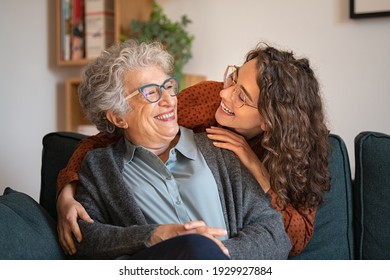 Old grandmother and adult granddaughter hugging at home and looking at each other. Happy senior mother and young daughter embracing with love on sofa. Happy woman hugging from behind grandma with love