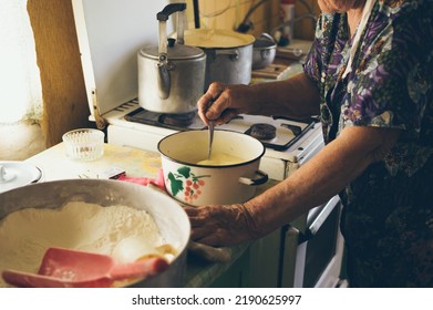 Old Grandmother Kneads Dough For Pancakes In Saucepan