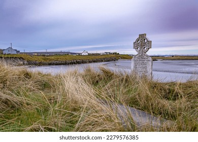 Old gravestone into deep windy grass by the shore close to the village in the distance