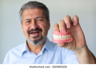 An old gray-haired man holds his denture. The man puts on the denture. Implant. Orthodontics. Old age. Teeth. Jaw. Advertising. The close plan. View from above. Removable denture.
